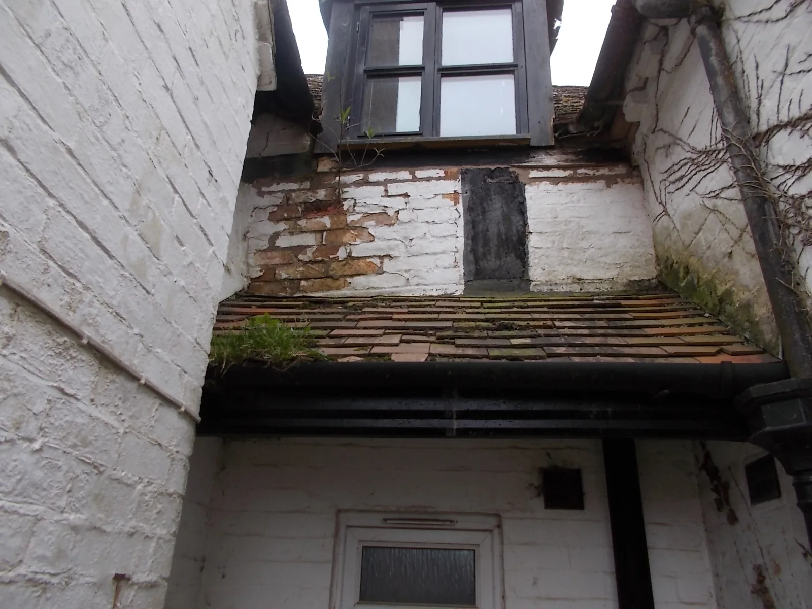 Failing roof tiles and brickwork with vegetation growing through