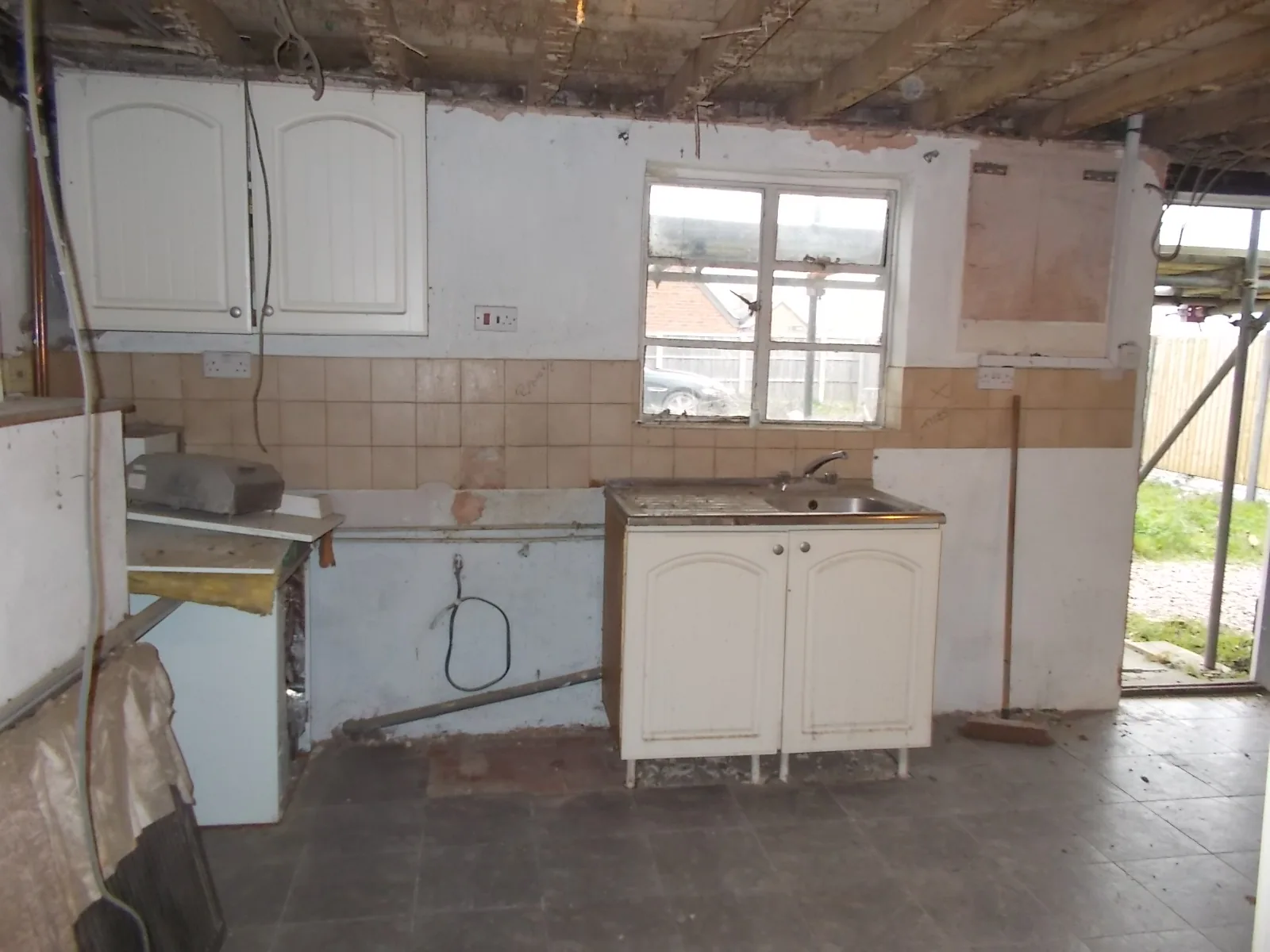 Original kitchen with dated units and sink, tiling part-removed and ceiling opened up